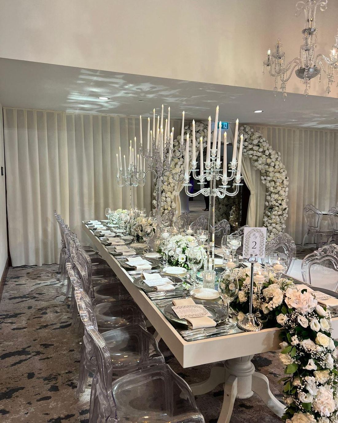 Mirrored long table with ghost chairs and a circular floral backdrop