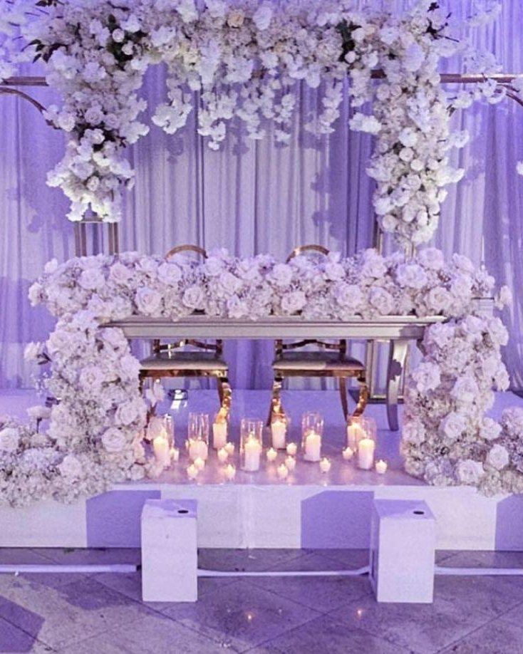 Sweetheart table on a candle-lined stage beneath a floral arch