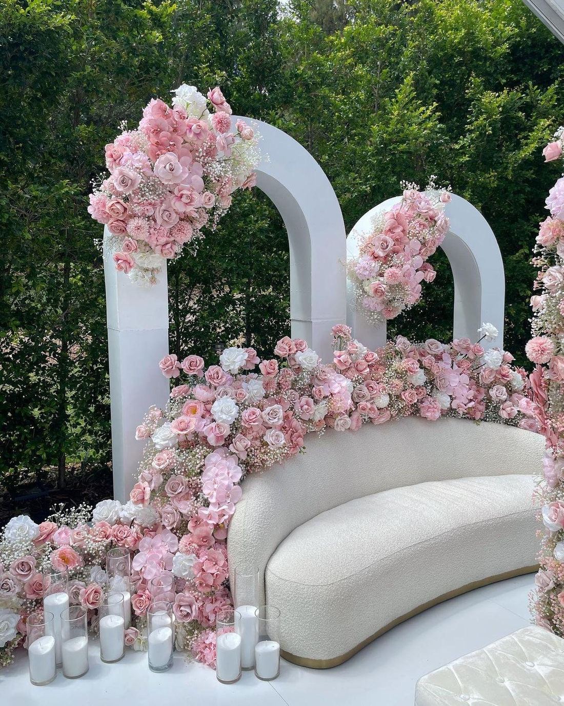Outdoor floral arch installation with a cream sofa and pastel roses