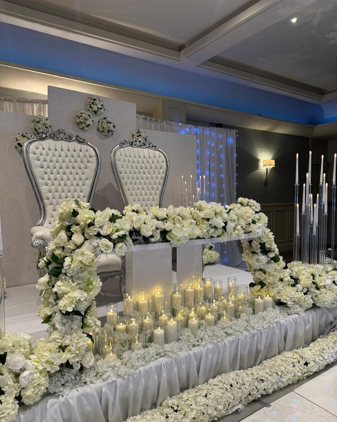 Bride and groom throne chairs framed by an all-white floral installation